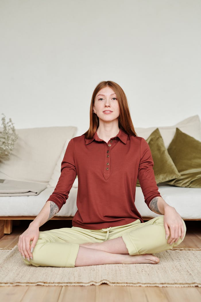 Woman in Red Long Sleeve Shirt Sitting on Brown Rug near White Sofa